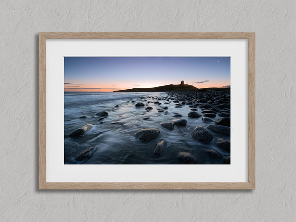 Ethereal Dawn coastal wall art featuring Northumbrian castle ruins, rocky shoreline and calm sea at sunrise