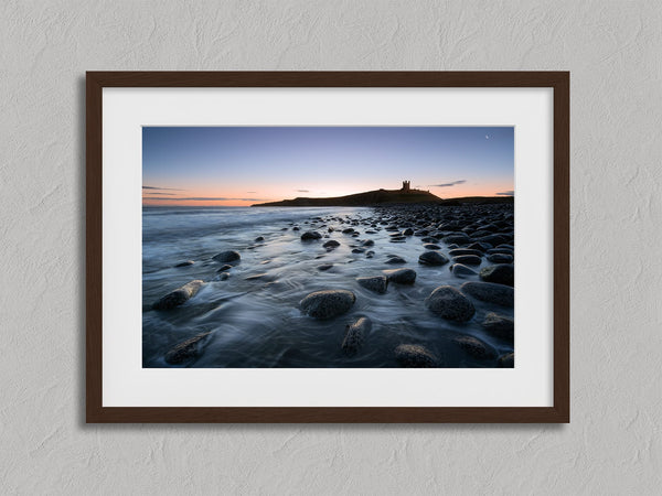 Ethereal Dawn coastal wall art featuring Northumbrian castle ruins, rocky shoreline and calm sea at sunrise