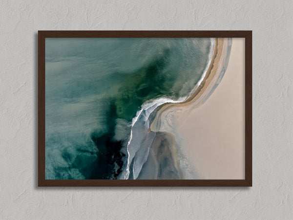 Aerial coastal view of deep teal water curling into pale sand along a sweeping shoreline.
