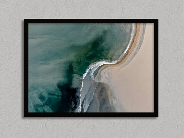 Aerial coastal view of deep teal water curling into pale sand along a sweeping shoreline.