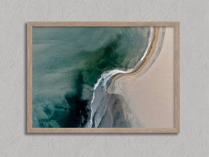 Aerial coastal view of deep teal water curling into pale sand along a sweeping shoreline.