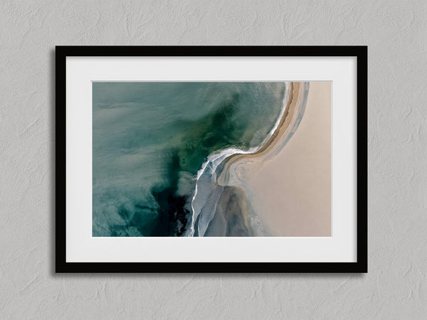 Aerial coastal view of deep teal water curling into pale sand along a sweeping shoreline.