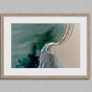 Aerial coastal view of deep teal water curling into pale sand along a sweeping shoreline.