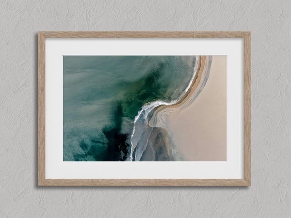 Aerial coastal view of deep teal water curling into pale sand along a sweeping shoreline.