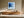 Black-framed blue abstract print above a long wooden sideboard in a sunlit space.