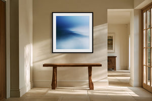 Black-framed blue abstract print above a rustic wooden bench in a bright hallway.