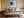 Black-framed blue abstract print centered above a bed with layered neutral bedding.
