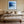 Black-framed blue abstract print centered above a bed with layered neutral bedding.