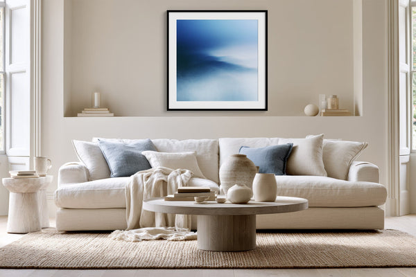 Black-framed blue abstract print above a white sofa with pale blue cushions.