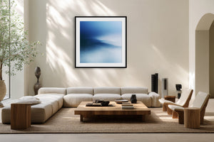 Black-framed blue abstract print above a low cream sectional and wooden coffee table.