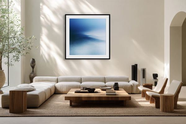Black-framed blue abstract print above a low cream sectional and wooden coffee table.