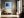 Black-framed blue abstract print above a bench with an orange cushion near tall windows.
