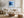 Black-framed blue abstract print above a white sofa, round wood table, and woven ottoman.