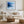 Black-framed blue abstract print above a white sofa, round wood table, and woven ottoman.