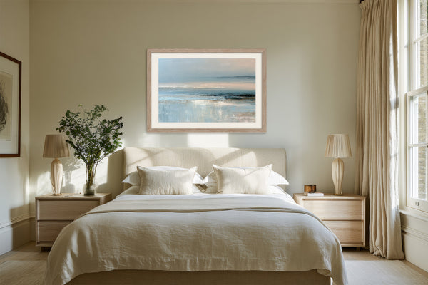 Pale blue coastal abstract in a light wood frame centered above a bed.