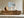 Light wood-framed coastal abstract hangs above a long wooden sideboard with ceramic vessels.