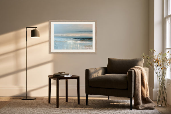 Framed pale blue coastal abstract above a dark armchair, side table, and floor lamp.