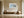 Light wood-framed coastal abstract above a wooden bench and round ceramic floor vase.