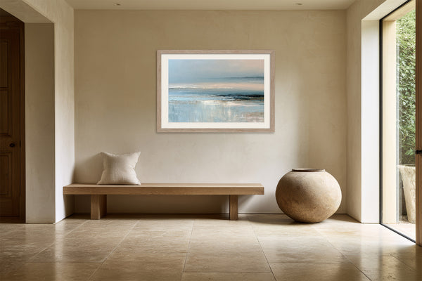 Light wood-framed coastal abstract above a wooden bench and round ceramic floor vase.