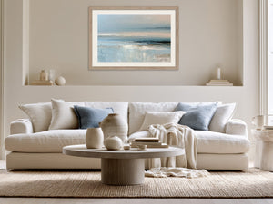 Light wood-framed coastal abstract above a white sofa with pale blue cushions.