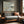 Pale Estuary abstract landscape in a slim wood frame above a gray sofa beside a window.