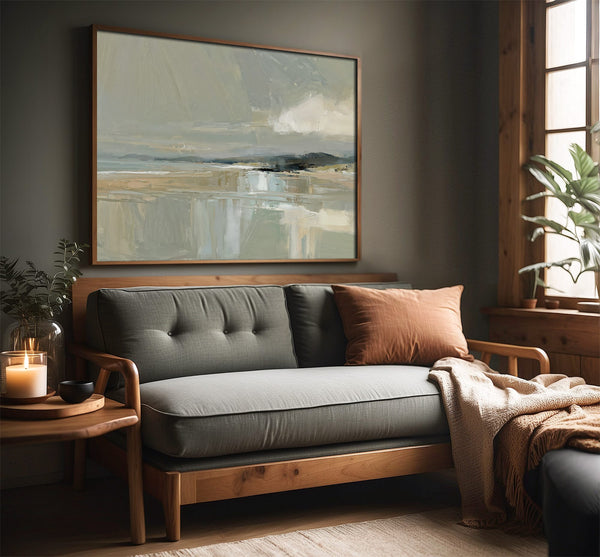 Pale Estuary abstract landscape in a slim wood frame above a gray sofa beside a window.