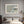 Pale Estuary print with a white mat and light wood frame above a bed near a fireplace.