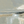 Abstract estuary landscape with pale water, sand and a dark low horizon in muted blue-grey and sage tones.