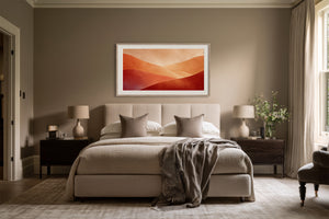White-framed abstract dune artwork centered above a bed with neutral bedding and bedside tables.