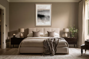 Framed grey and black abstract artwork centered above a bed with neutral bedding.