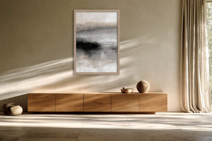 Framed grey and charcoal abstract artwork above a low wooden sideboard in sunlight.