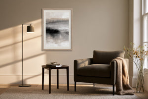 Framed abstract landscape above a dark armchair, side table, and floor lamp.