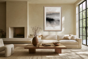 Framed abstract landscape above a cream sofa and wooden coffee table near large windows.