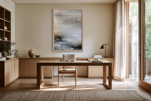 Framed grey, beige, and charcoal abstract artwork above a wooden desk and chair.