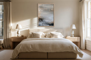 Framed layered abstract artwork centered above a bed with cream bedding and bedside lamps.