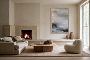 Framed grey and charcoal abstract artwork above a low ledge beside a lit fireplace.