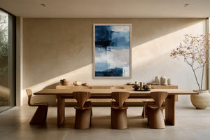 Vertical blue and white abstract artwork in a light wood frame above a long dining table.