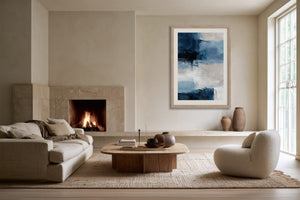 Blue and white abstract wall art in a light wood frame above a fireplace seating area.