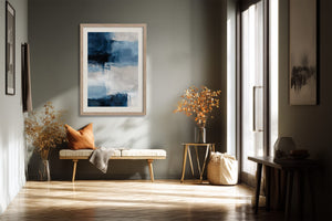 Blue and white abstract artwork in a light wood frame above a bench with an orange cushion.