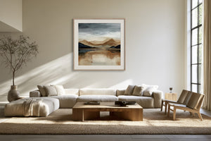Framed mountain lake artwork displayed above a white sectional sofa and wood coffee table.