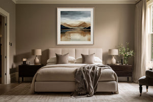 White-framed mountain lake artwork centered above a bed between dark wood nightstands.