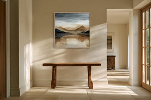 Framed mountain lake artwork above a rustic wood bench in a sunlit hallway.