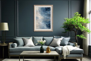 Framed blue and white abstract artwork above a gray sofa in a dark paneled living room.