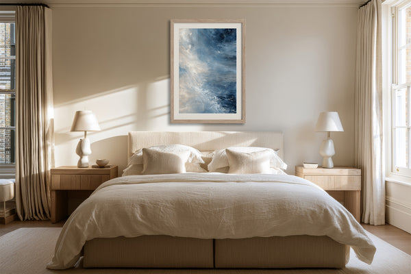 Framed blue and white abstract artwork centered above a bed between matching bedside lamps.