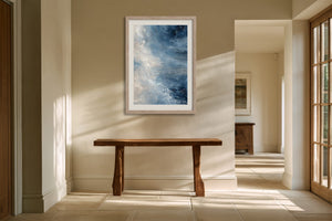 Blue and white abstract artwork in a light wood frame above a rustic console table.