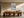Framed abstract seascape centered above a long wooden dining table and sculptural chairs.