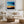 Black-framed abstract sunset print above a white sofa with pillows and a round wood coffee table.