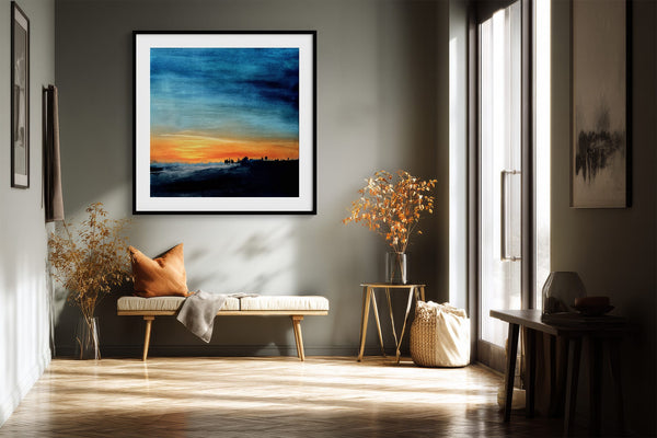 Black-framed abstract sunset print above a bench with an orange cushion and dried branches.