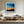 Black-framed abstract sunset print above a cream sectional sofa and low wood coffee table.