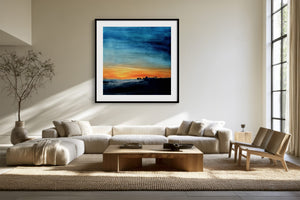 Black-framed abstract sunset print above a cream sectional sofa and low wood coffee table.